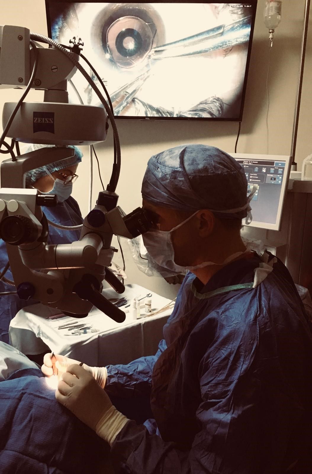 Dr. William Wiley at the surgical microscope during a cataract procedure, the operative view displayed on the monitor beside him